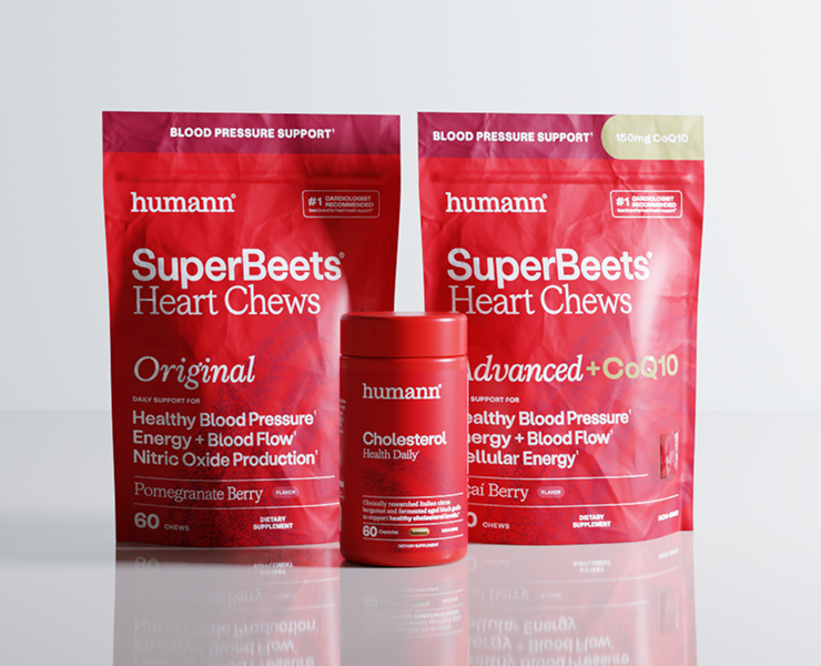 Three red Humann SuperBeets Heart Chews supplement packages on a light gray reflective background: one large pouch labeled Original, one large pouch labeled advanced+CoQ10, and one smaller cylindrical jar labeled Cholesterol Health Daily.