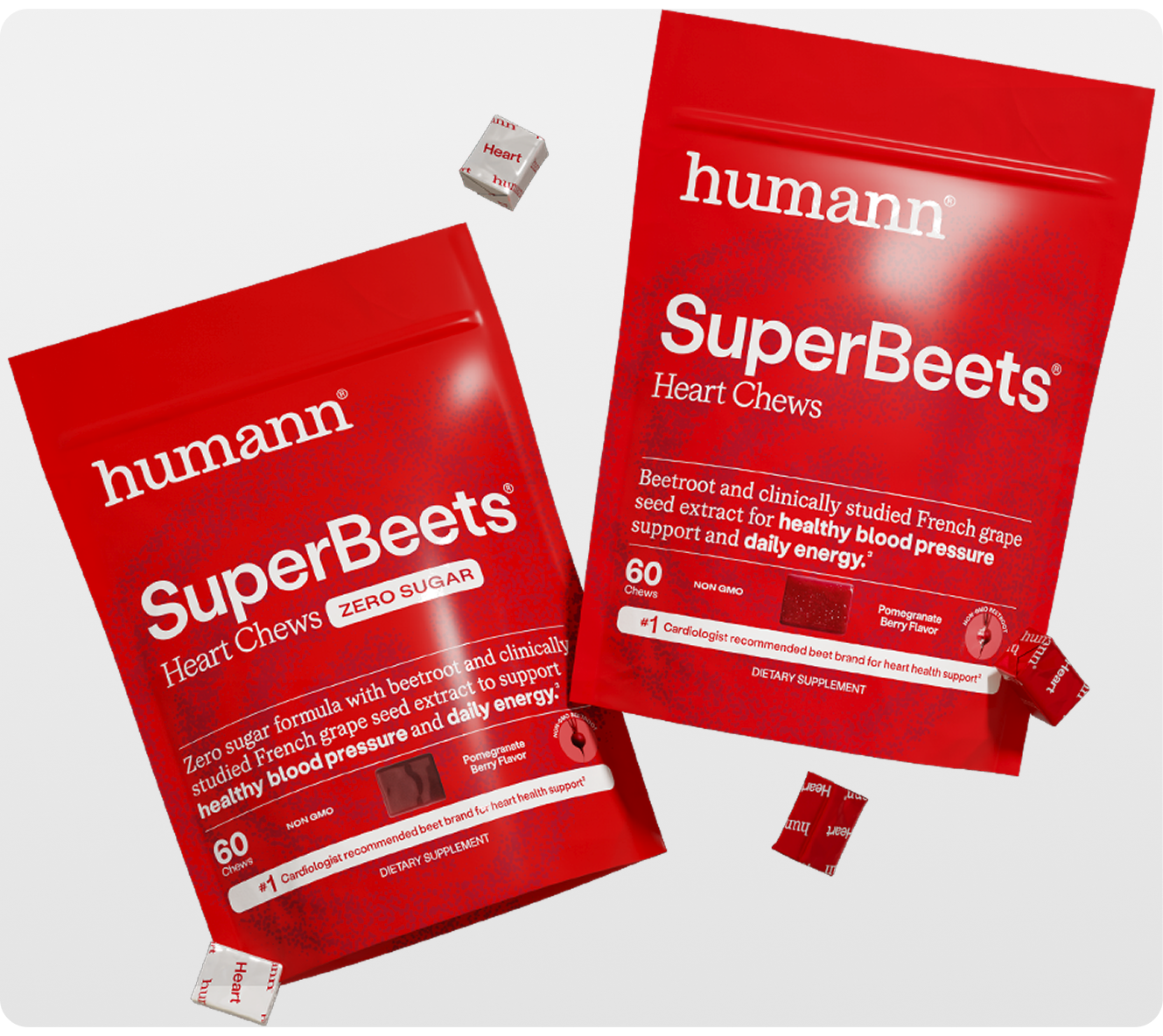 Two red Humann SuperBeets Heart Chews stand-up pouches on a light gray background, with a few individual red chews scattered nearby.
