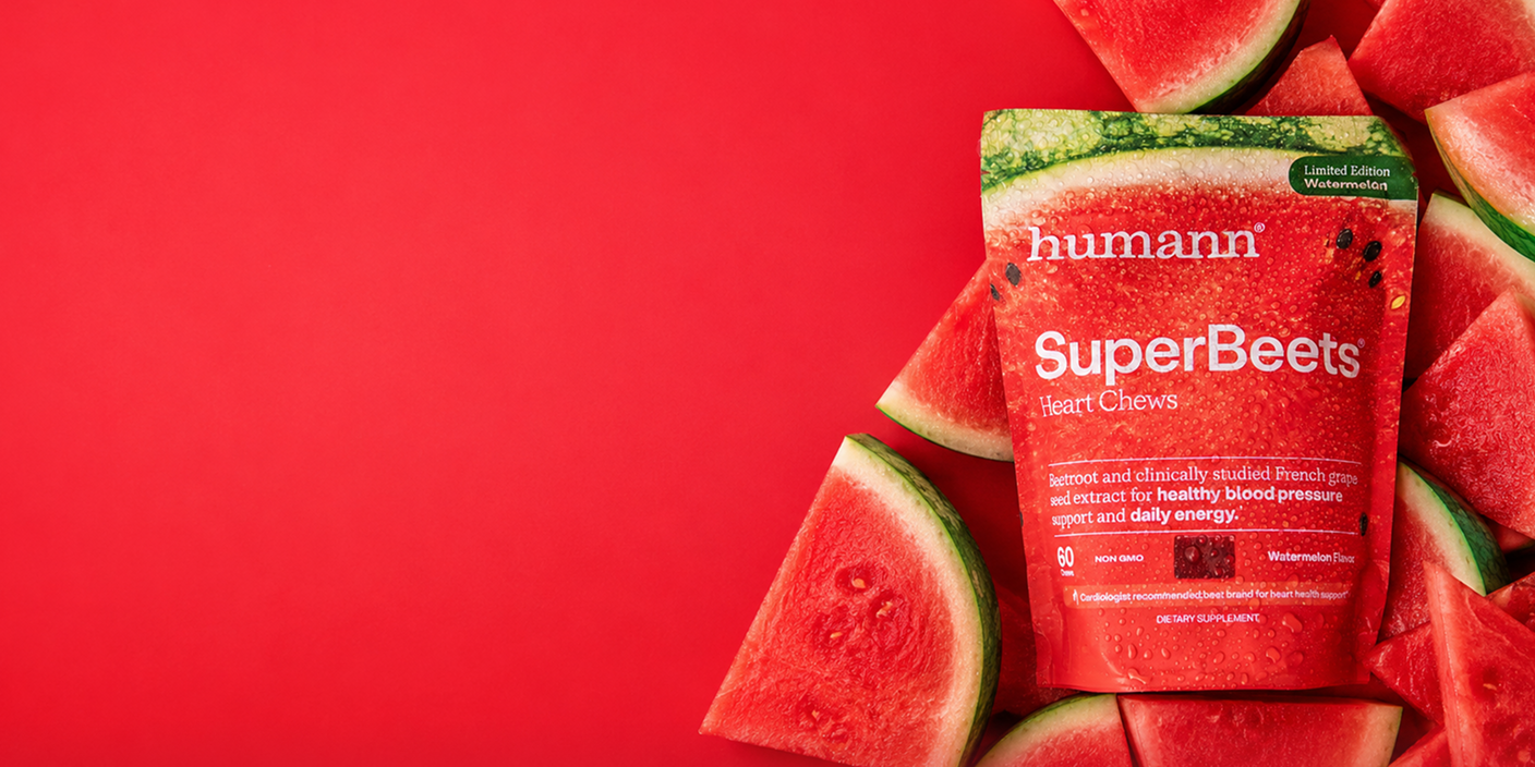 A package of Humann SuperBeets Heart Chews watermelon flavor surrounded by fresh watermelon slices on a solid red background.