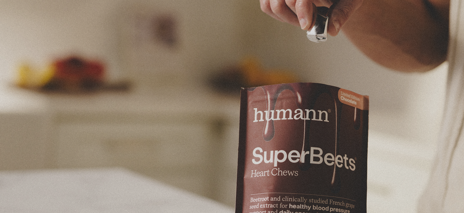 Person holding a package of humann SuperBeets Chocolate Heart Chews in a kitchen setting.