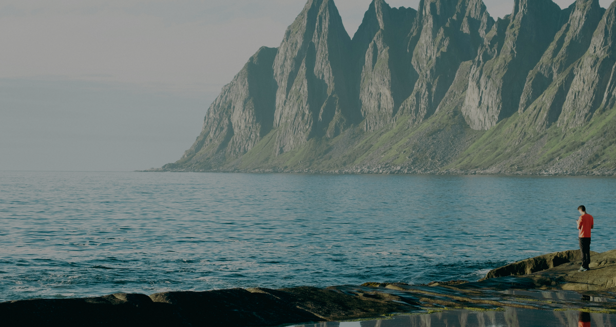 Person standing on a rocky shoreline below steep green mountains