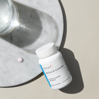 Bottle Active B-Complex supplement with a pill on a marble surface.